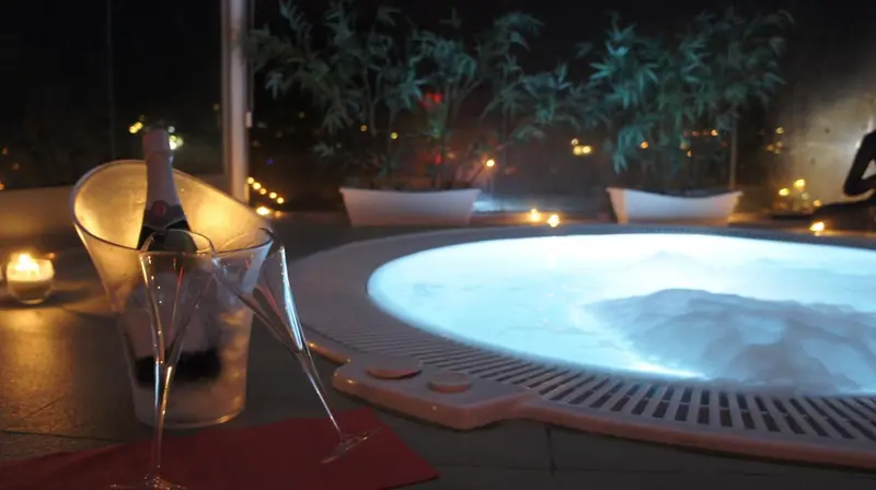 Une bouteille de champagne et un verre sont posés près d'un jacuzzi éclairé.