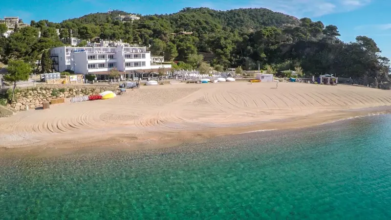 Vue aérienne d'une plage de sable fin bordée d'une eau turquoise et d'un bâtiment blanc.