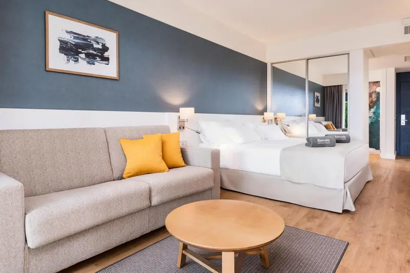 Une chambre lumineuse avec un canapé gris et un grand lit blanc.