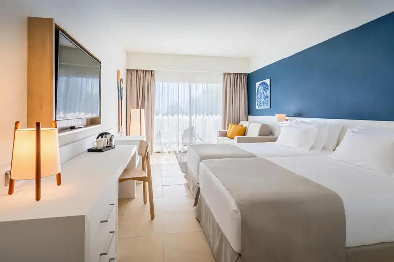 Chambre lumineuse avec deux lits et vue sur l'extérieur.