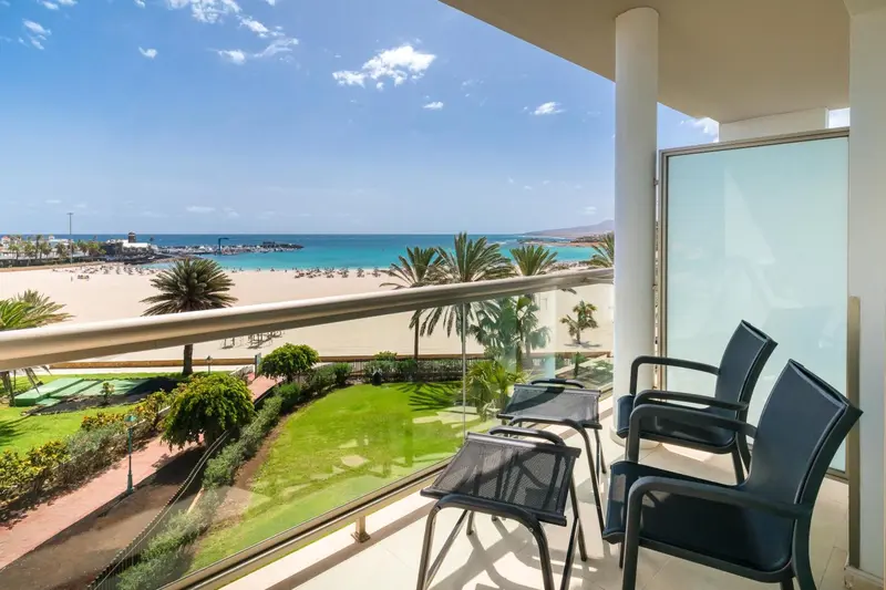 Terrasse avec mobilier d'extérieur donnant sur une plage de sable fin et une mer bleue.