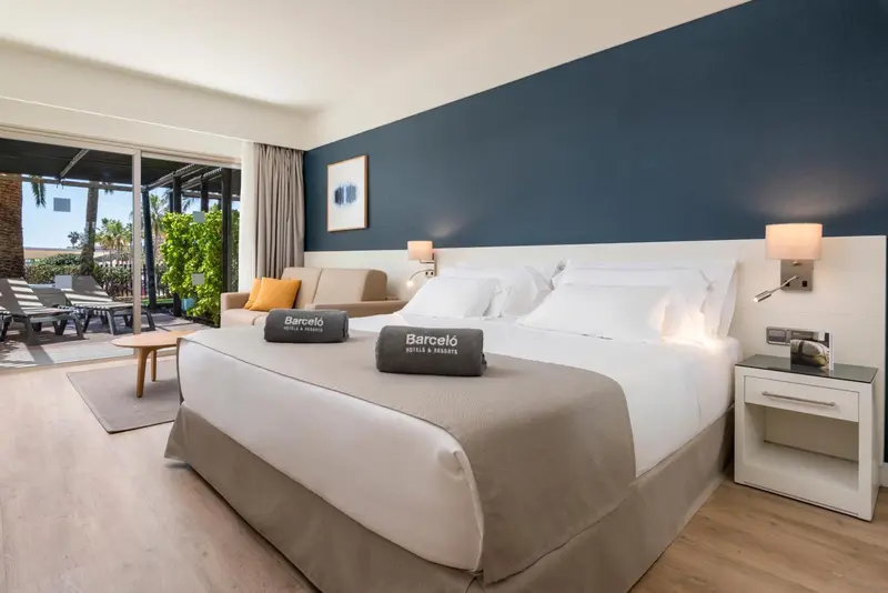 Une chambre lumineuse avec un grand lit et un canapé face à une baie vitrée.