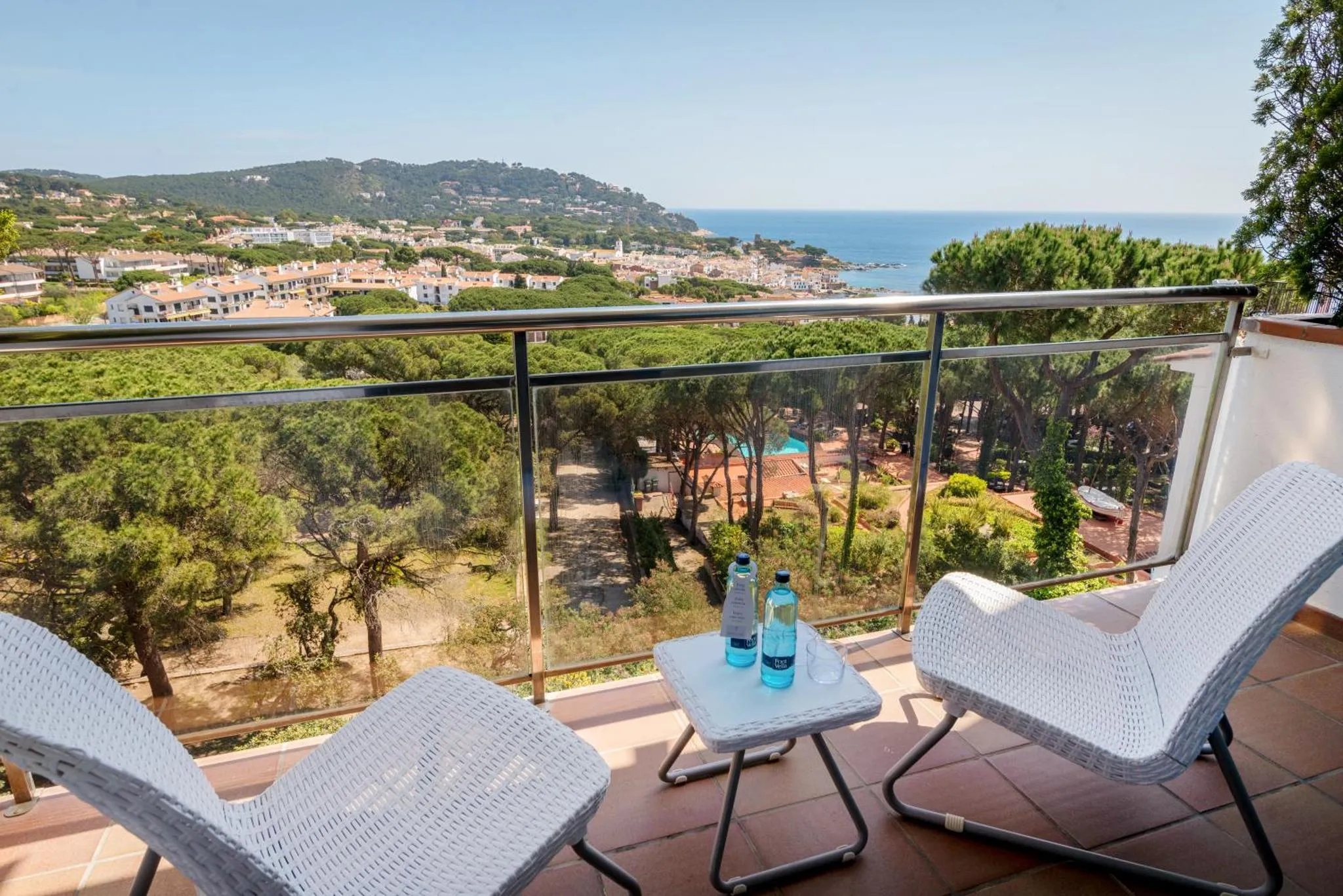 Deux fauteuils blancs sur une terrasse avec vue sur la mer et la végétation.