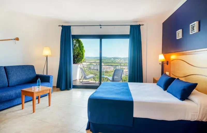 Chambre lumineuse avec canapé bleu et vue sur un paysage verdoyant.