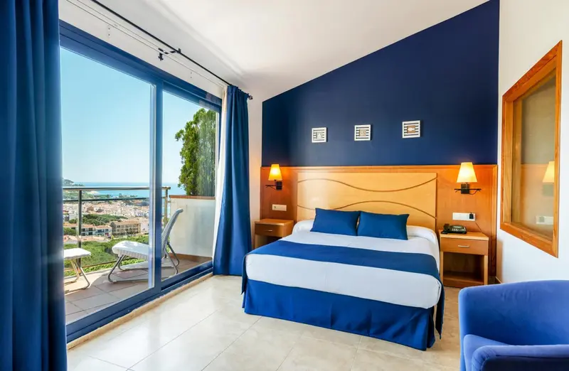 Chambre lumineuse avec un lit double et un balcon offrant une vue sur la mer.