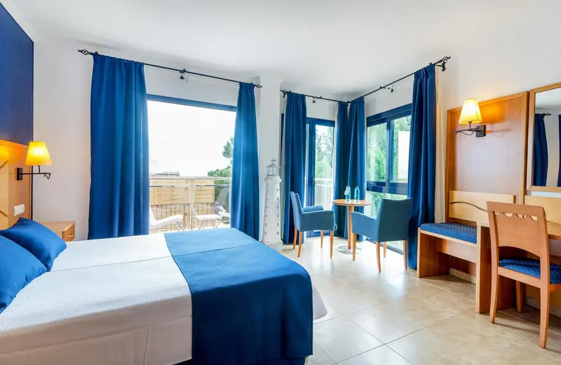 Une chambre lumineuse avec un lit double et un coin repas près d'une baie vitrée.