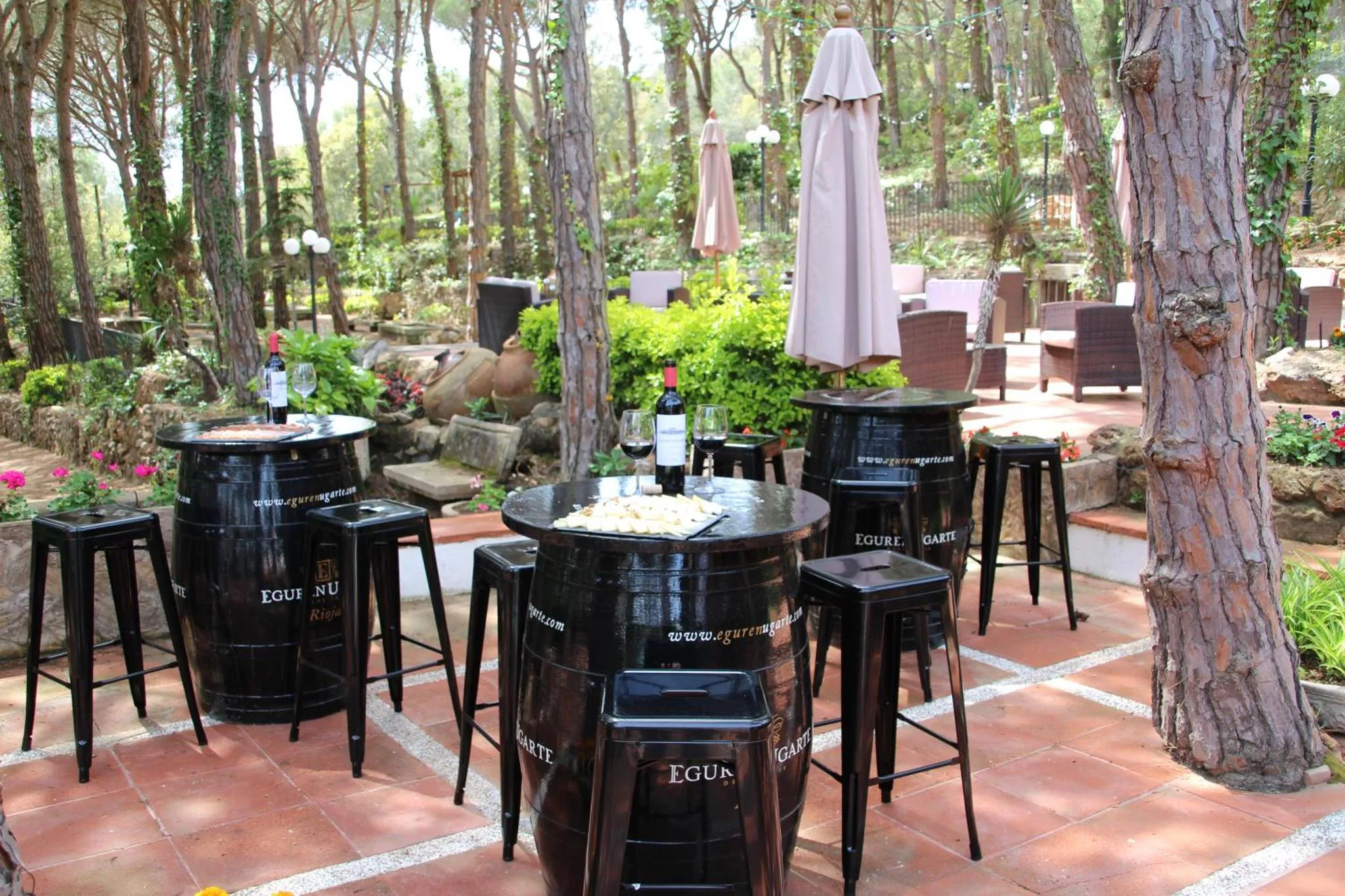 Tables et chaises en métal disposées sur une terrasse pavée ombragée par des arbres.