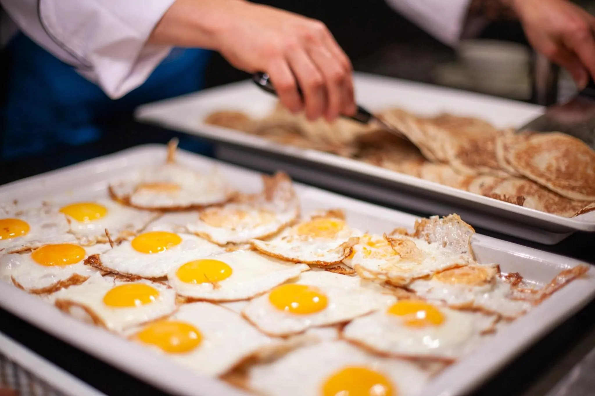 Un plateau d'oeufs au plat et de crêpes est préparé par un chef.