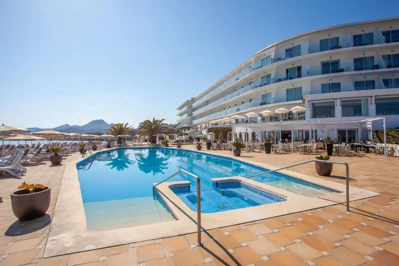 Vue d'une piscine devant un bâtiment blanc avec des transats et des parasols.