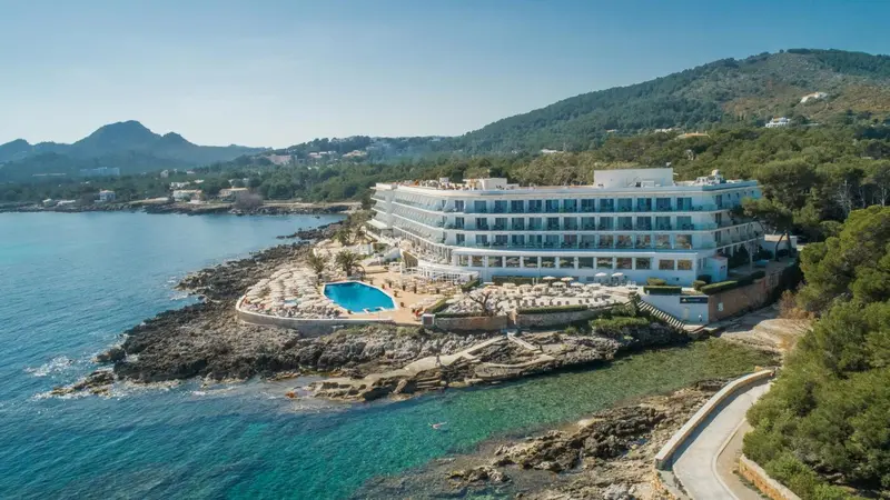 Vue aérienne d'un bâtiment blanc surplombant une crique rocheuse et une piscine.