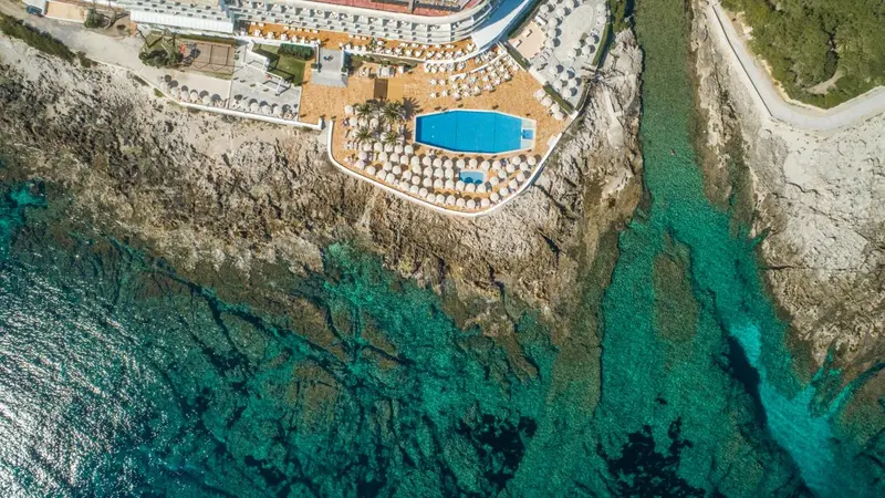 Vue aérienne d'un complexe hôtelier avec piscine et transats au bord de l'eau turquoise.