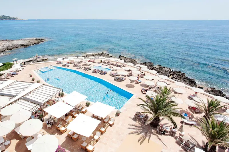 Vue aérienne d'une piscine bordée de transats et d'une plage rocheuse.