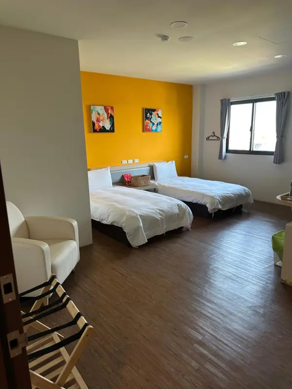 Chambre lumineuse avec deux lits simples et un fauteuil.