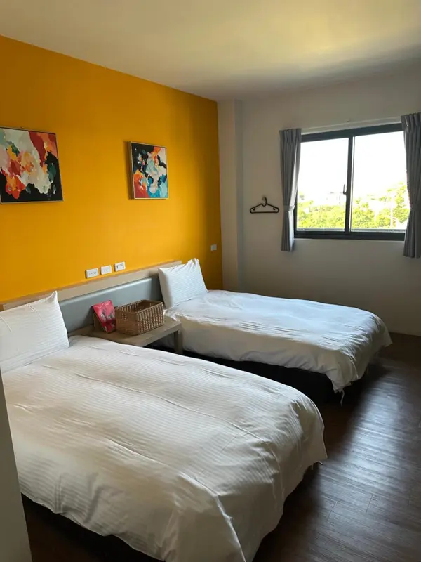 Chambre lumineuse avec deux lits simples et un tableau coloré au mur.