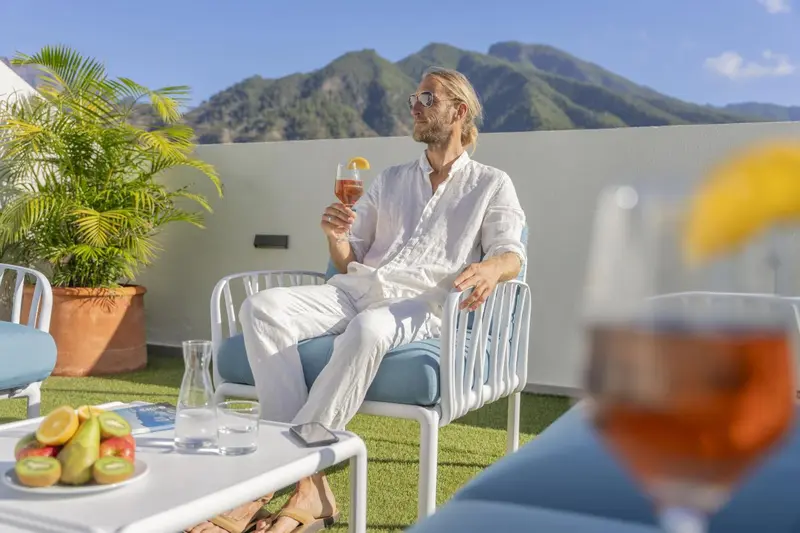 Un homme se détend sur une terrasse avec un cocktail et une vue sur les montagnes.
