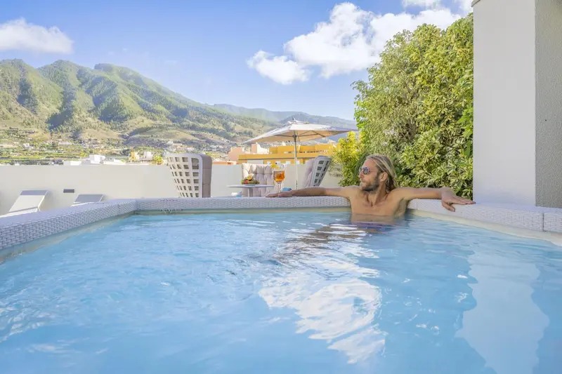 Un homme se détend dans une piscine sur une terrasse ensoleillée avec vue sur les montagnes.