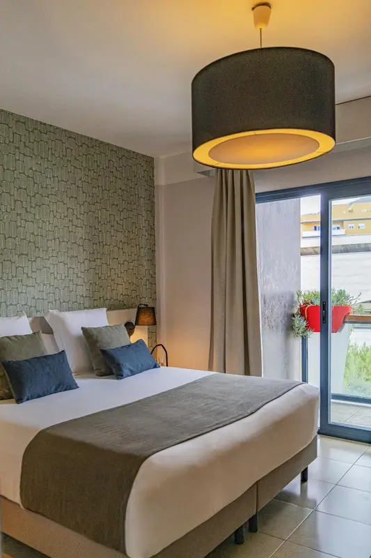 Une chambre lumineuse avec un grand lit et un accès à un balcon.