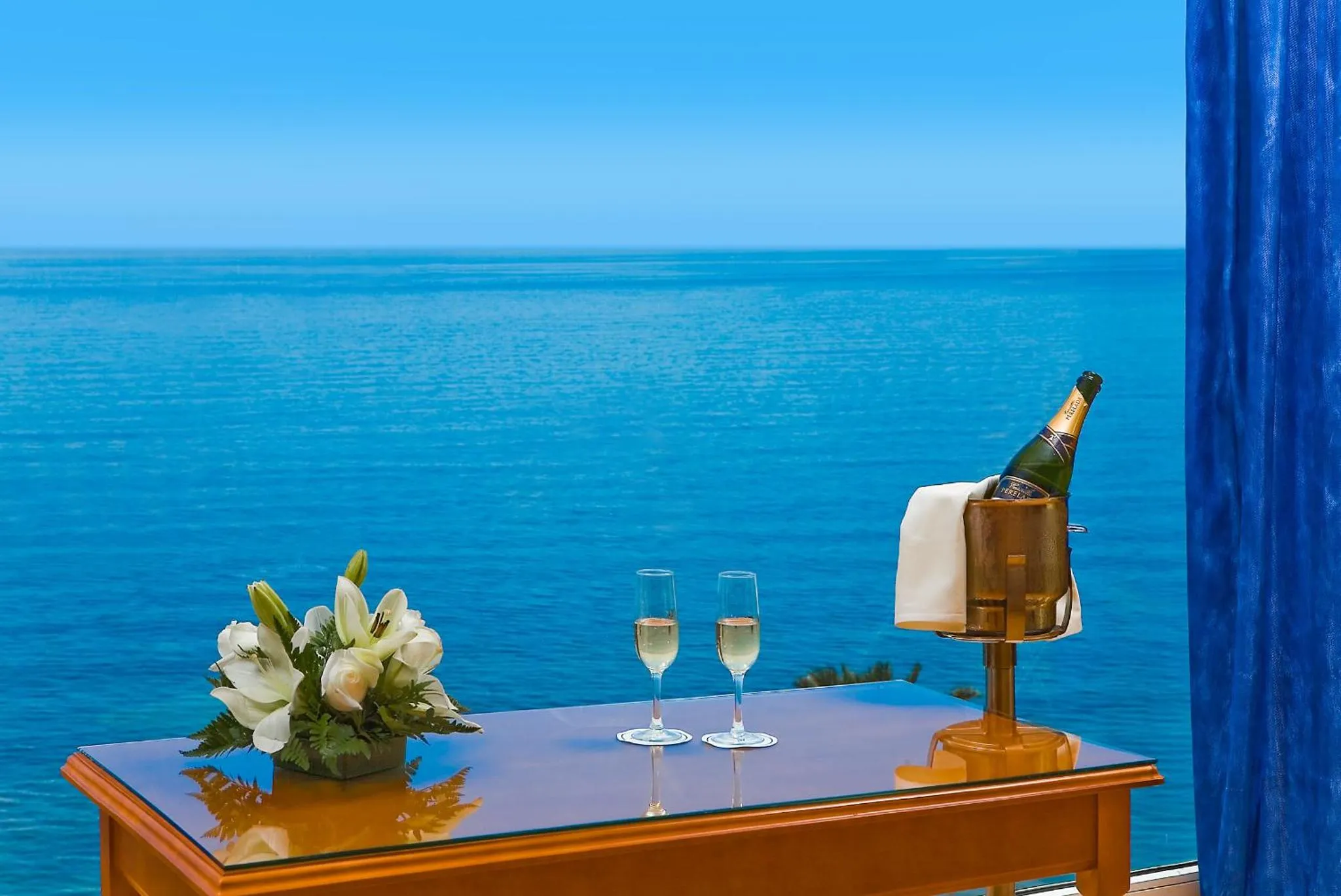 Une table avec une bouteille de champagne et deux verres est mise en scène devant une vue sur la mer.