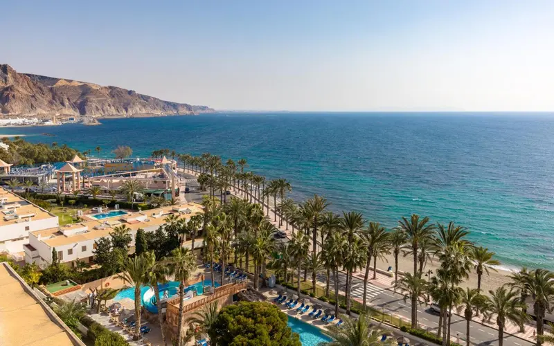 Vue aérienne d'un complexe hôtelier avec piscine et palmiers le long d'une plage.