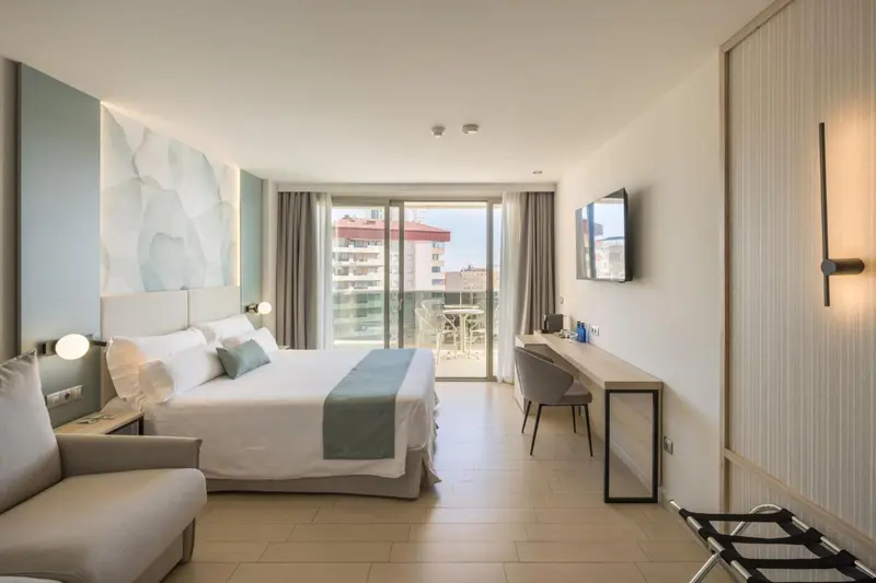 Une chambre lumineuse avec un grand lit et un bureau donnant sur une vue extérieure.