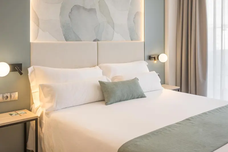 Une chambre lumineuse avec un grand lit recouvert de draps blancs et d'un oreiller vert.