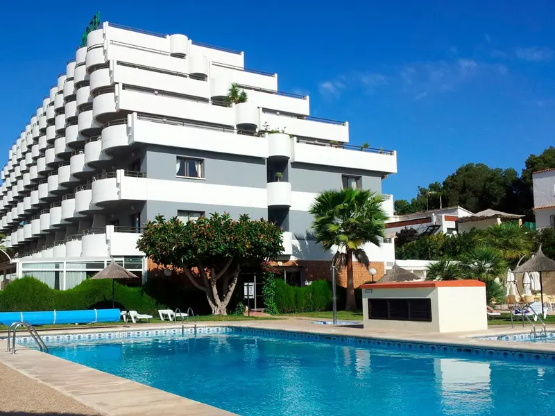 Bâtiment blanc à plusieurs étages surplombant une piscine et une pelouse verdoyante.