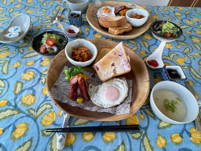 Une table est dressée avec un petit-déjeuner copieux composé d'œufs, de saucisses, de pain grillé et de salades.
