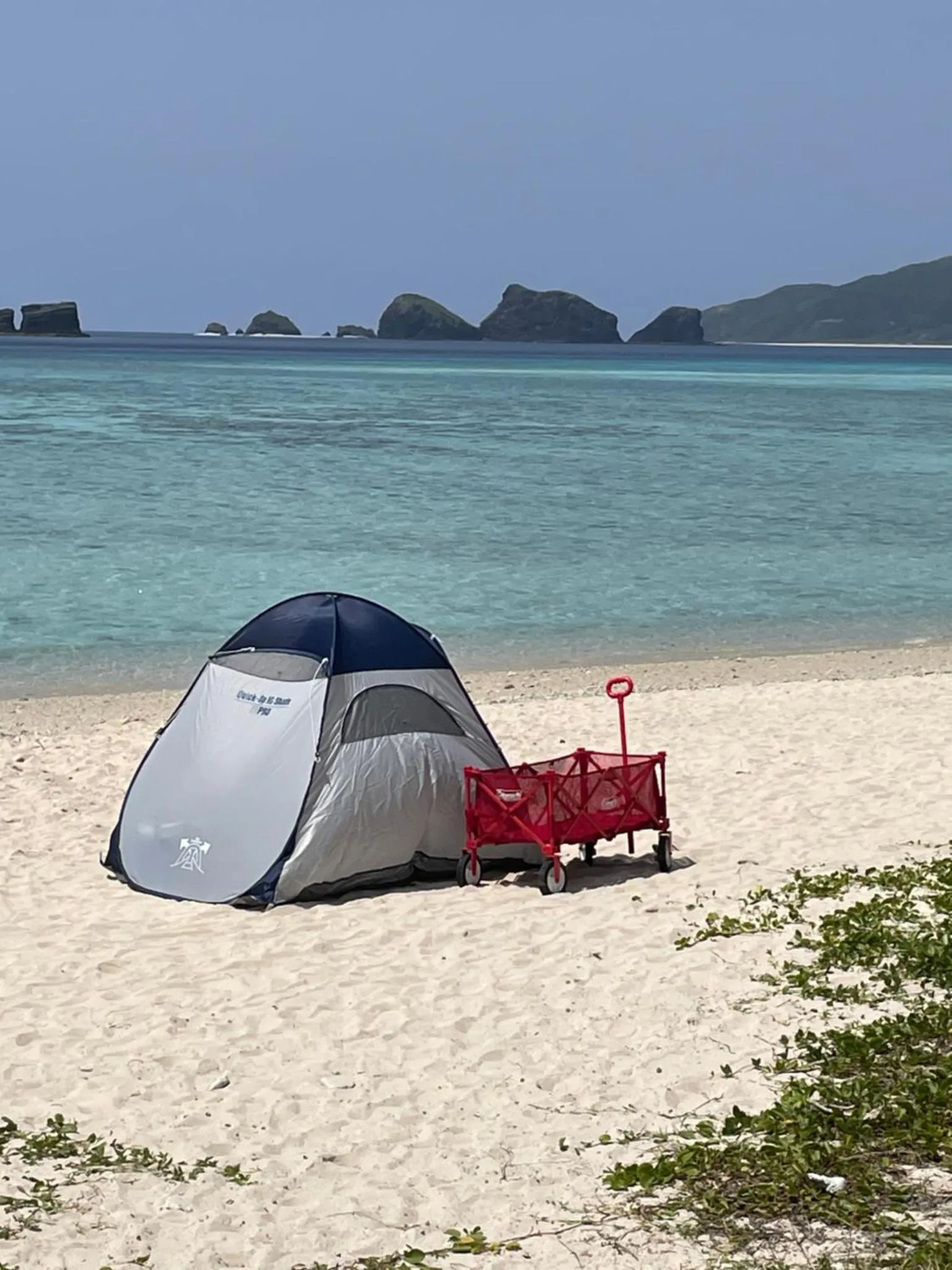 Une tente de plage et une charrette reposent sur le sable clair face à la mer.