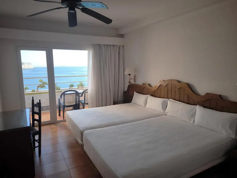 Chambre lumineuse avec vue sur la mer depuis un balcon.