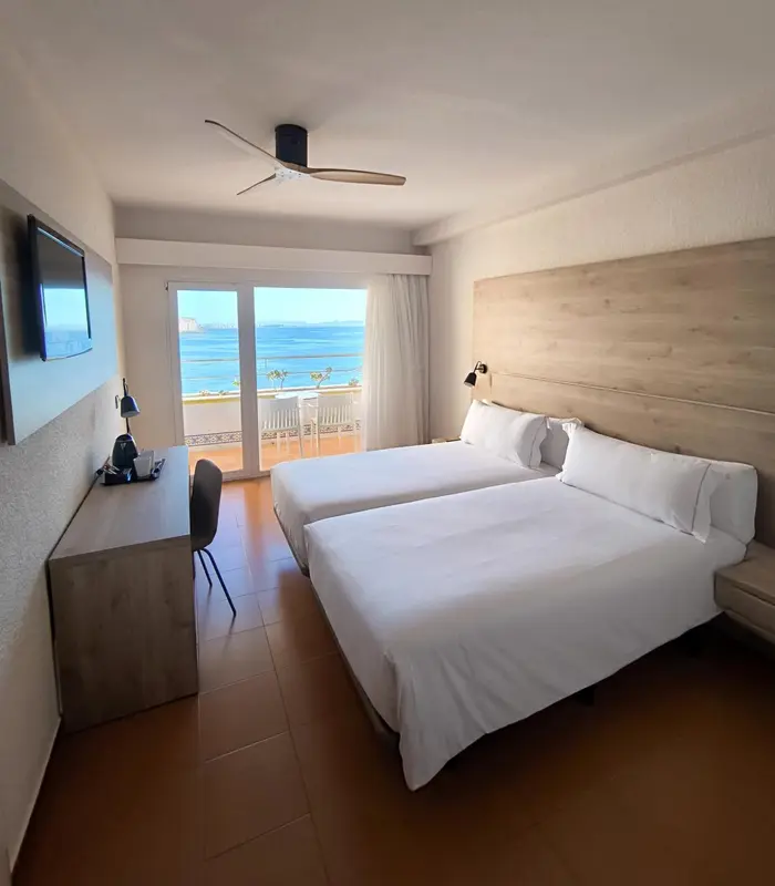 Chambre lumineuse avec un grand lit et vue sur la mer.