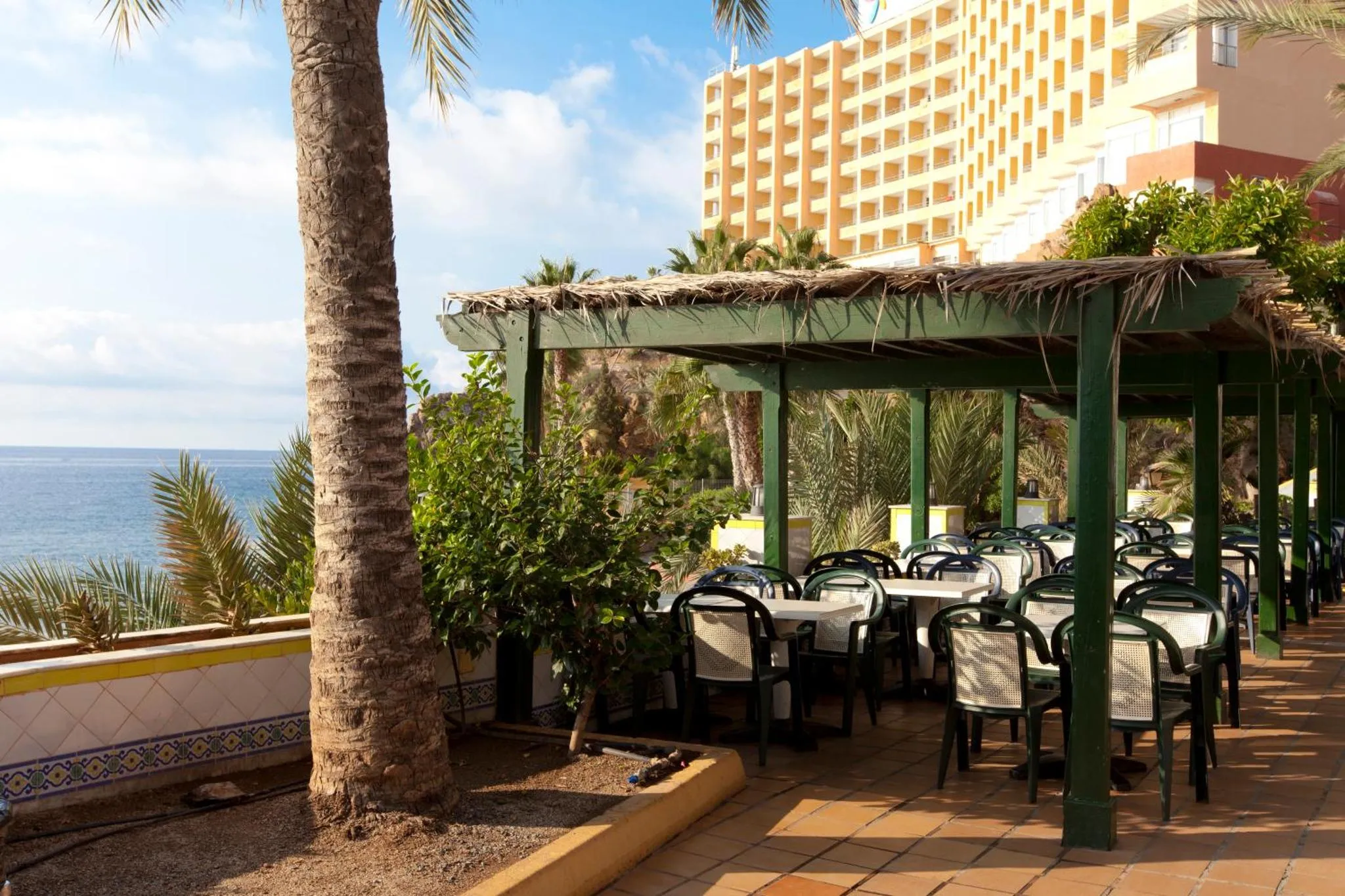 Terrasse ombragée avec tables et chaises donnant sur la mer.