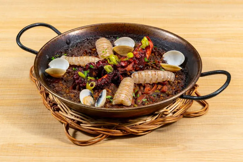 Une paella aux fruits de mer est présentée dans une poêle en métal sur un support en osier.