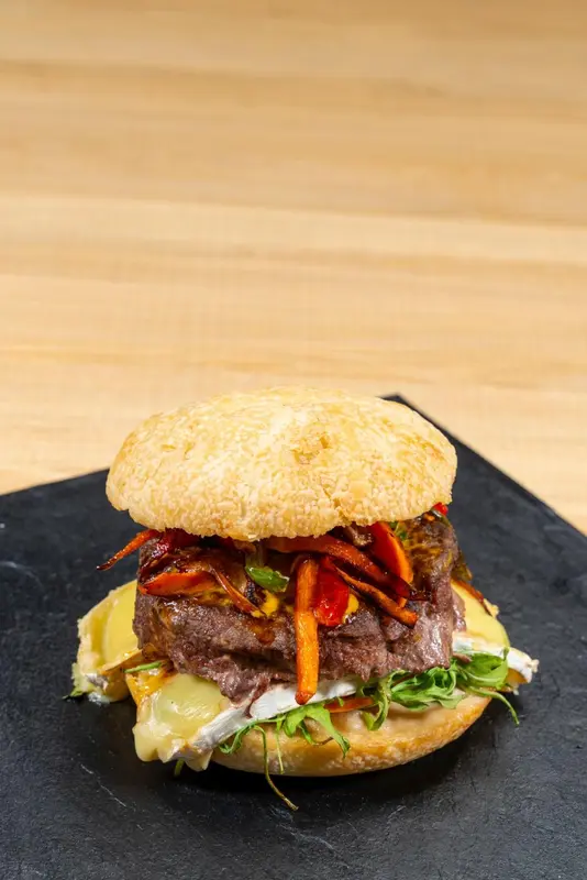 Un hamburger garni est présenté sur une ardoise noire.
