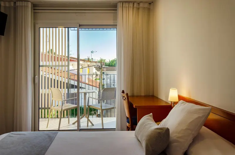 Une chambre lumineuse s'ouvre sur un balcon avec vue sur la ville.