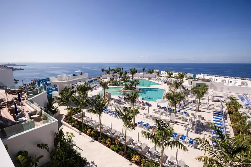 Vue aérienne d'un complexe hôtelier avec piscine et palmiers face à la mer.