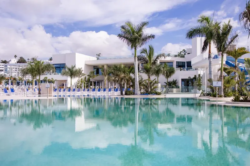 Vue d'une piscine turquoise bordée de transats devant un bâtiment blanc et moderne.