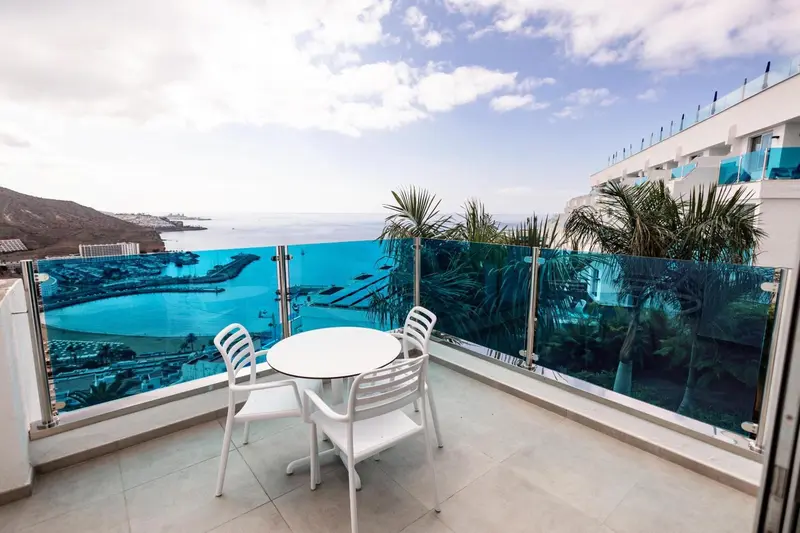 Terrasse avec mobilier blanc donnant sur une vue mer et un port de plaisance.