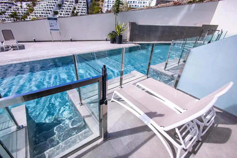 Transats blancs disposés au bord d'une piscine rectangulaire turquoise.
