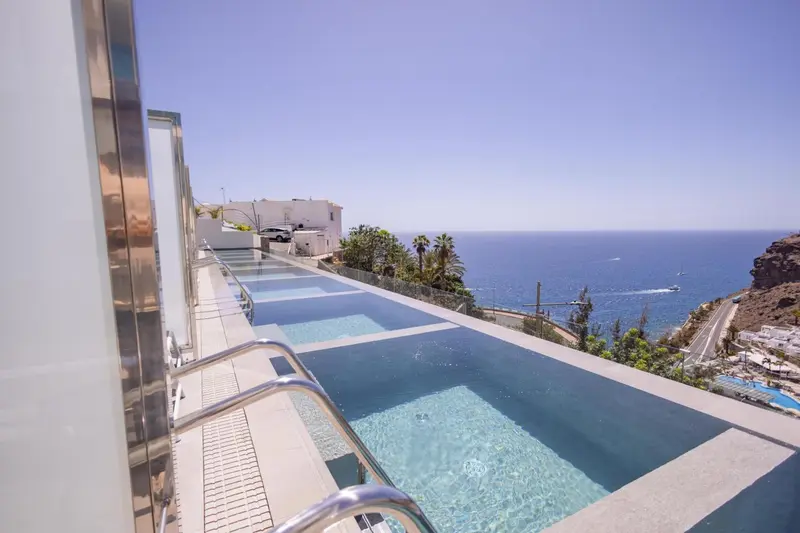 Une piscine à débordement offre une vue sur la mer et les bâtiments environnants.