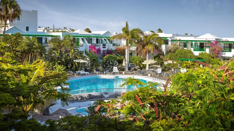 Vue d'une piscine d'hôtel entourée de végétation luxuriante et de bâtiments blancs.