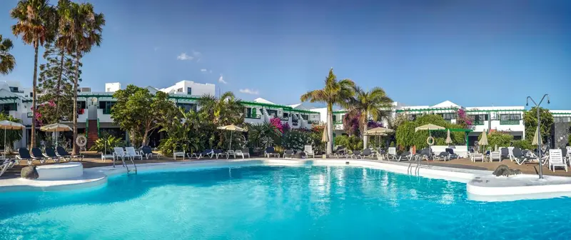 Vue d'une piscine d'hôtel bordée de transats et de palmiers sous un ciel bleu.