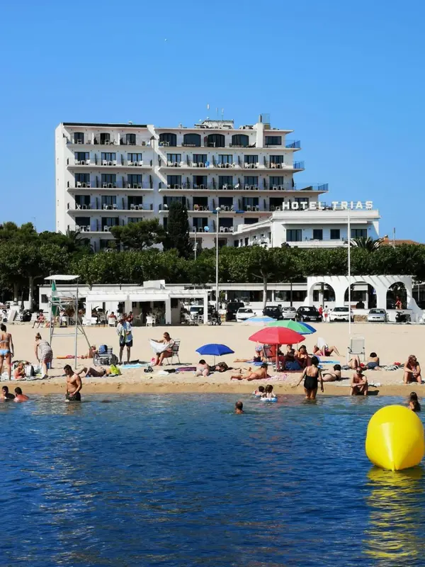 Vue d'une plage ensoleillée avec des transats et des parasols devant un bâtiment blanc.