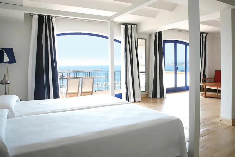 Une chambre lumineuse avec un grand lit blanc donnant sur une vue mer.