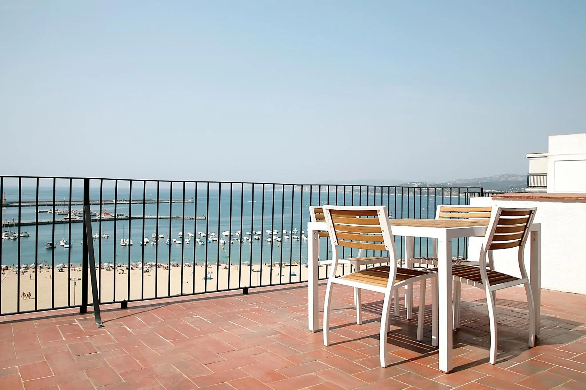 Terrasse avec mobilier en bois et vue sur la mer et un port.