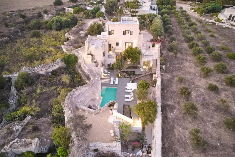 Vue aérienne d'une propriété blanche avec piscine et végétation luxuriante.