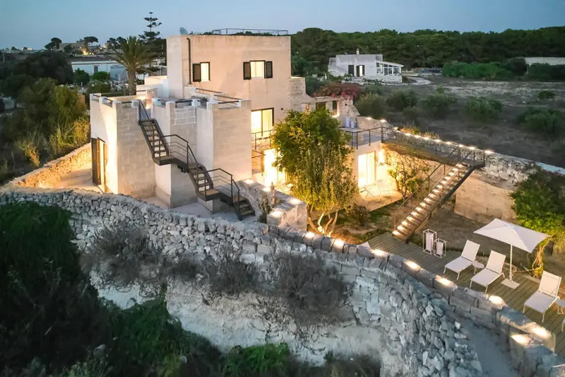 Bâtiment moderne éclairé au crépuscule avec des escaliers extérieurs et des chaises longues.
