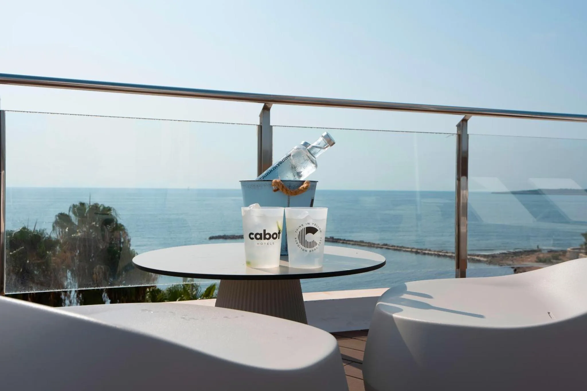 Une table ronde avec des verres et une bouteille sur une terrasse avec vue sur la mer.