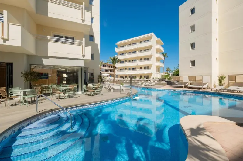 Une piscine turquoise reflète les bâtiments blancs et le ciel bleu.