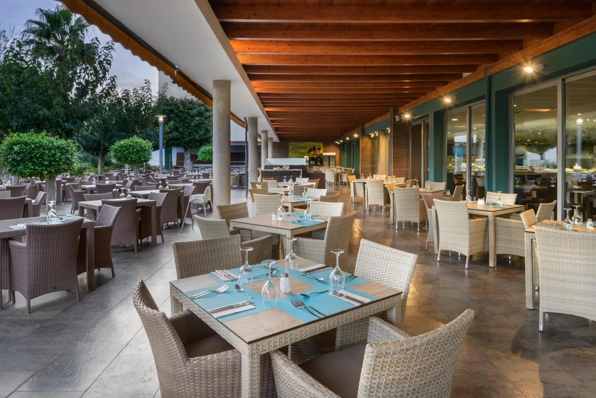 Une salle à manger extérieure avec des tables dressées et des chaises en osier.
