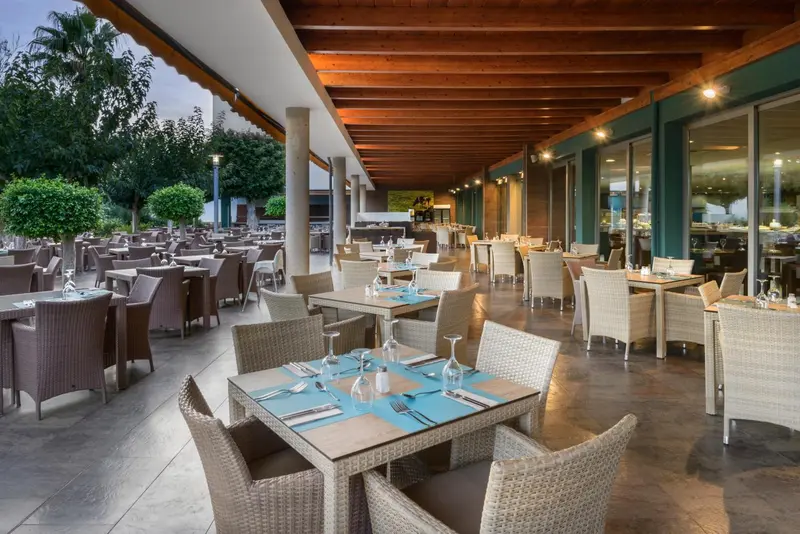 Une salle à manger extérieure avec des tables dressées et des chaises en osier.